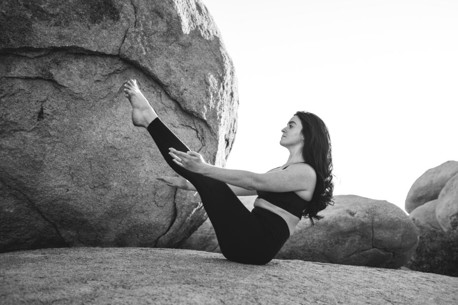 grayscale photo of woman exercising on top of large rock